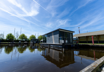Modern houseboat at Marina Heeg in the Netherlands, reflected in calm water under a bright blue sky.