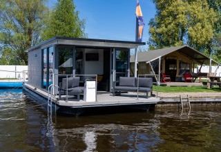Et foto af Houseboat Heeg ved Marina Heeg i Holland, med terrasse og sofaer ved vandet.