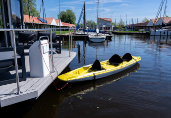 Gelbes Kajak am Hausboot am Marina Heeg, Niederlande, mit Segelbooten und Wasser im Hintergrund.