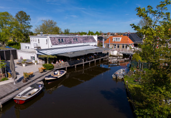 Houseboat at Marina Heeg, Netherlands, with a terrace by the canal, small boats, and clear blue sky.