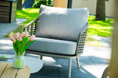 Sillón exterior gris con cojín y jarrón de tulipanes en Wood Cottage, De Witte Berg, Países Bajos.