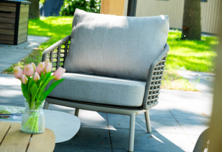 Sillón exterior gris con cojín y jarrón de tulipanes en Wood Cottage, De Witte Berg, Países Bajos.
