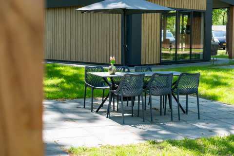 Buitenzithoek bij Wood Cottage in vakantiepark De Witte Berg, Nederland, met tafel, stoelen en parasol.