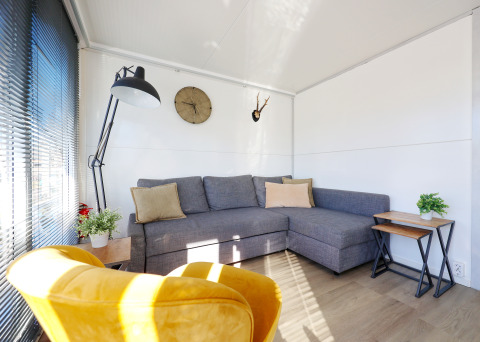Modernes Wohnzimmer auf dem Hausboot De Hoop in Marina Parcs mit grauem Sofa, gelbem Sessel und Deko.