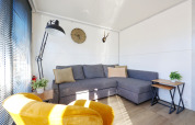 Modernes Wohnzimmer auf dem Hausboot De Hoop in Marina Parcs mit grauem Sofa, gelbem Sessel und Deko.