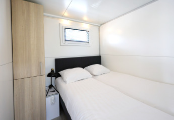 Dormitorio en la casa flotante 'De Hoop' en Marina Parcs con dos camas, armario y pequeña ventana.