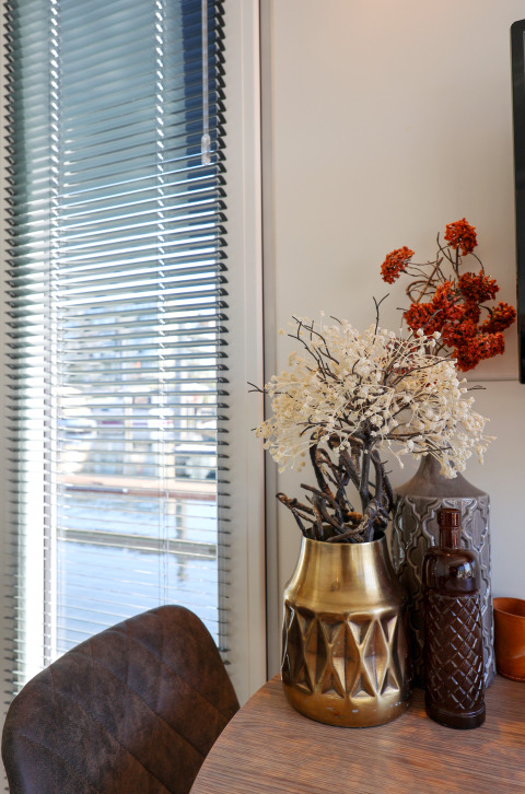 Living area on houseboat De Hoop with vases and table, window blinds, and marina view in the Netherlands.