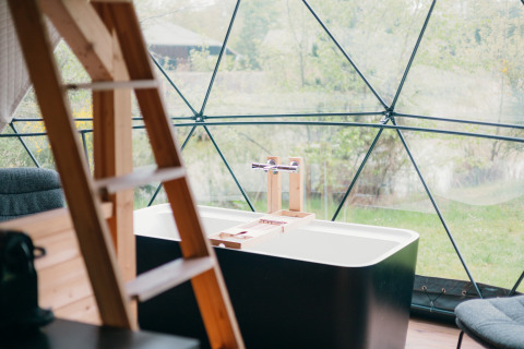 Bañera y escalera de madera dentro de una tienda domo redonda con vistas panorámicas a la naturaleza en Holanda.