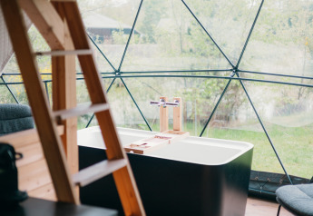 Badkuip en houten ladder in een ronde glamping tent met panoramisch uitzicht op de natuur in Nederland.