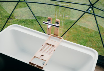 Baignoire moderne avec plateau en bois sous dôme vitré offrant vue sur pelouse à Sallandshoeve, Pays-Bas.