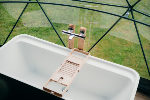 Baignoire moderne avec plateau en bois sous dôme vitré offrant vue sur pelouse à Sallandshoeve, Pays-Bas.