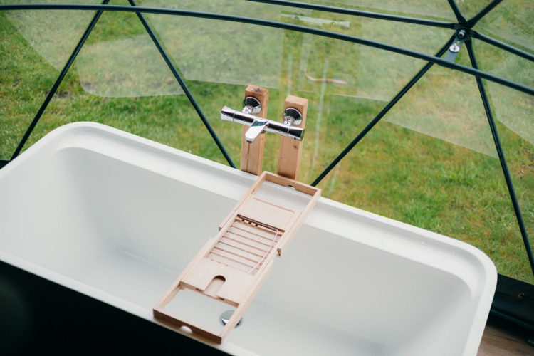 Bañera moderna y bandeja de madera en domo de cristal con vista al césped, Round Holly Tent, Sallandshoeve.