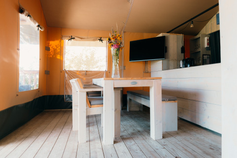 Comedor con mesa y bancos de madera dentro de una tienda safari en Holiday Park Sallandshoeve, Países Bajos.