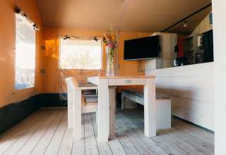 Eethoek met houten tafel en banken binnen een safaritent bij Holiday Park Sallandshoeve, Nederland.