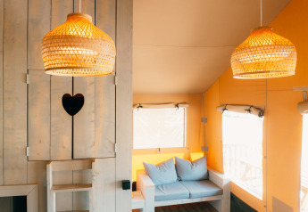 Intérieur du Safari cottage avec lampes en osier, cœur décoratif et canapé bleu au Holiday Park Sallandshoeve.