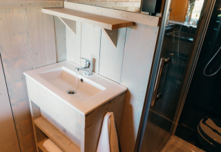 Moderne badeværelse med hvid håndvask, hylder og glasdør i Safari cottage, Sallandshoeve, Holland.