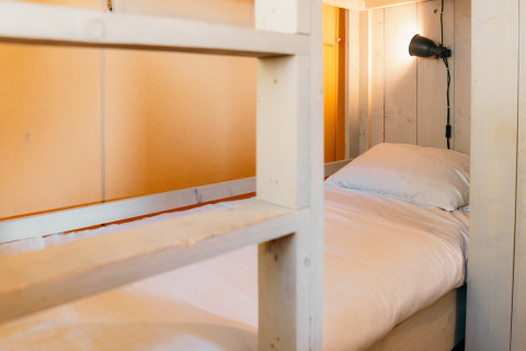 Vue intérieure d’un lit avec draps blancs et lampe de lecture dans un cottage safari à Sallandshoeve, Pays-Bas.