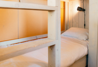 Vista interior de una cama con sábanas blancas y lámpara de lectura en una cabaña safari en Sallandshoeve, Países Bajos.