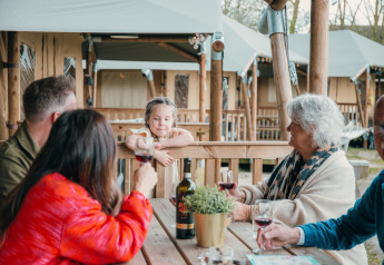 Familie nyder vin udenfor en safaricottage i Ferienpark Sallandshoeve, Holland, med et barn smilende.