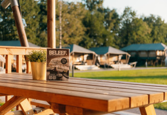 Safari cottage ved Holiday Park Sallandshoeve i Holland med træbord, brochure og plante udenfor.