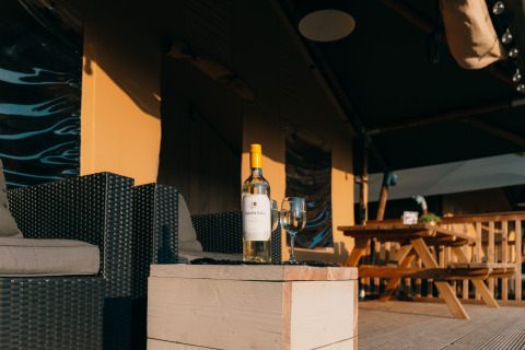 Bottiglia di vino e bicchiere su tavolo davanti alla tenda Safari Cottage a Holiday Park Sallandshoeve, Olanda.