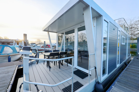 Moderne Hausboot mit Terrasse und Glasfront im Yachthafen De Hoop, Niederlande, bei Sonnenuntergang.