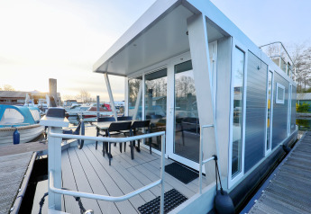 Moderne husbåd med terrasse og glasdøre ved Marina Parcs - Jachthaven De Hoop i Holland ved solnedgang.