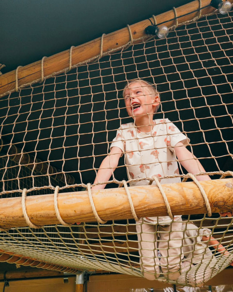 Child playing on a rope net in the Ranger Lodge safari tent at Holiday Park Sallandshoeve, Netherlands.