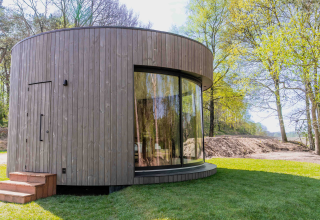 Casa pequeña circular Lumni Pod con gran ventana curva en Wilsumer Berge, Alemania, entre árboles.