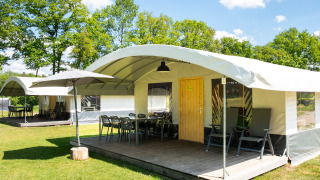 Safaritent Tentvilla op recreatiepark De Witte Berg in Nederland met terras, stoelen en parasol.