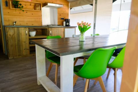 Dining area with green chairs and rustic kitchen inside Tentvilla safari tent at De Witte Berg, Netherlands.