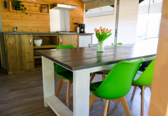 Dining area with green chairs and rustic kitchen inside Tentvilla safari tent at De Witte Berg, Netherlands.