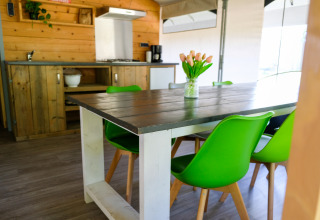 Comedor con sillas verdes y cocina rústica en la tienda Tentvilla en el parque De Witte Berg, Países Bajos.