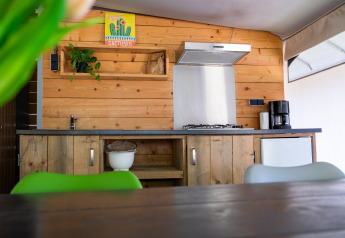 Moderne tekøkken i safari-telt på De Witte Berg, med træpaneler, kaffemaskine og grønne stole.