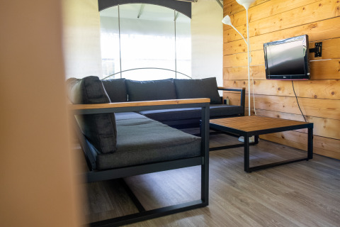 Moderne opholdsstue i en safaritelttent på Holiday park De Witte Berg med grå sofa og trævæg.