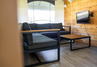 Moderne opholdsstue i en safaritelttent på Holiday park De Witte Berg med grå sofa og trævæg.