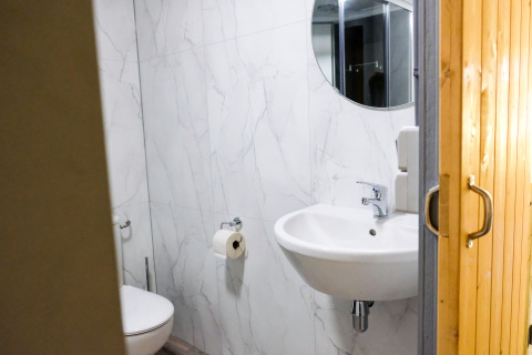 Salle de bains moderne avec murs effet marbre blanc, miroir rond et porte en bois dans la tente Tentvilla.