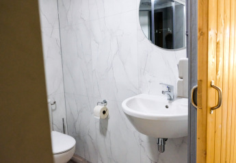 Modernes Badezimmer mit weißer Marmorwand, rundem Spiegel und Holztür im Safari-Zelt Tentvilla.