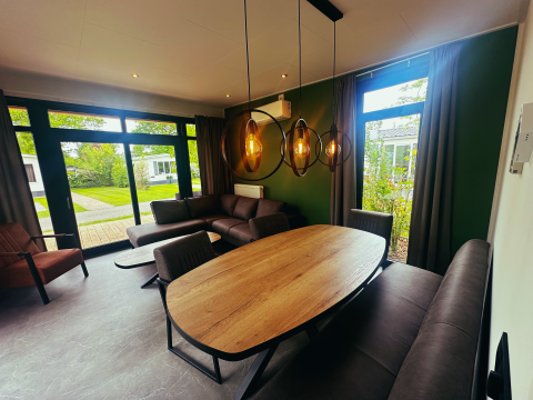 Moderne leef- en eetruimte bij Sunlodge in vakantiepark 't Rheezerwold, Nederland, met grote ramen en tuinzicht.
