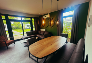 Moderne leef- en eetruimte bij Sunlodge in vakantiepark 't Rheezerwold, Nederland, met grote ramen en tuinzicht.