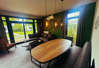 Modernes Wohnzimmer in der Sunlodge im Ferienpark 't Rheezerwold, Niederlande, mit großen Fenstern und Gartenblick.