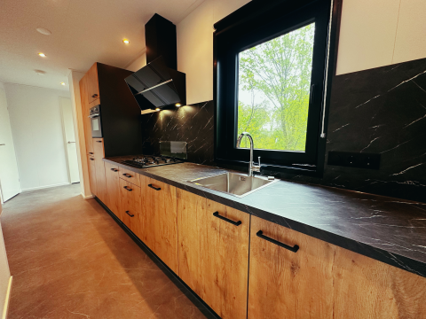 Moderne keuken met houten kasten, zwart werkblad en groot raam in een Sunlodge op Holiday Park 't Rheezerwold.
