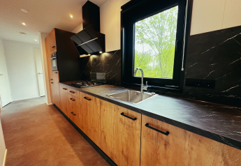 Moderne keuken met houten kasten, zwart aanrecht en groot raam in een Sunlodge op Holiday Park 't Rheezerwold.