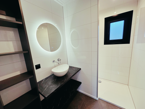 Moderne badkamer in Sunlodge bij Vakantiepark 't Rheezerwold, Nederland, met zwarte wastafel en rond spiegel.