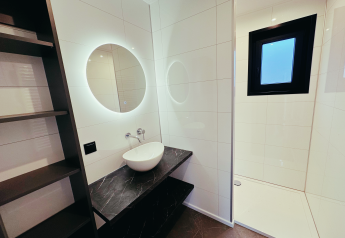 Modernes Badezimmer in der Sunlodge im Ferienpark 't Rheezerwold, Niederlande, mit schwarzer Ablage und rundem Spiegel.