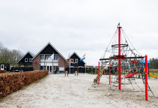 Spielplatz mit Klettergerüst und Rutsche vor einem Ferienparkgebäude in Drenthe, Niederlande, bei bewölktem Himmel.