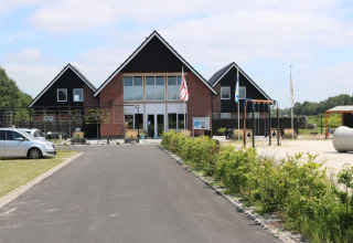 Ingresso al parco vacanze The Kremmer a Drenthe, Paesi Bassi, con edificio, area giochi e auto parcheggiate.