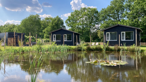 Zwei schwarze Ferienhütten am Teich im Ferienpark The Kremmer, Drenthe, Niederlande, sonniger Tag.