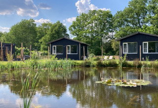 Zwei schwarze Ferienhütten am Teich im Ferienpark The Kremmer, Drenthe, Niederlande, sonniger Tag.