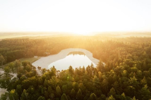 Vue aérienne d’un lac entouré de forêt au coucher du soleil dans le parc de vacances The Kremmer, Drenthe, Pays-Bas.